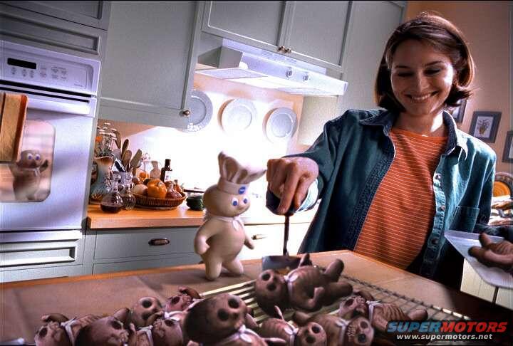woman in a kitchen smiles while holding a spatula over a Pillsbury Doughboy figure and a cooling rack of baked goods