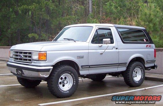 Silver Ford Bronco parked in a lot, trees in background