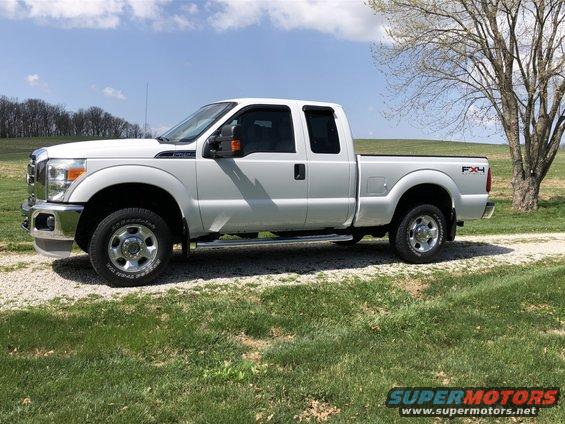 White 2011 Ford F-250 Super Duty pickup truck, side view, parked on gravel with grass and trees