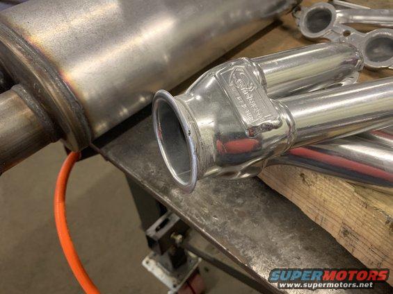 Close-up of a shiny metal exhaust pipe with some text stamped on it, resting on a workbench
