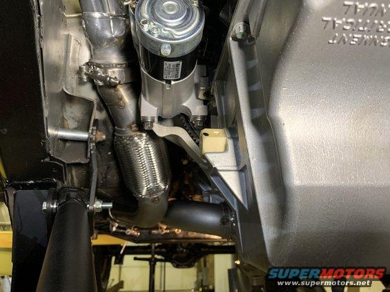 Close-up of a vehicle's starter motor and exhaust flex pipe, with part of the transmission housing visible