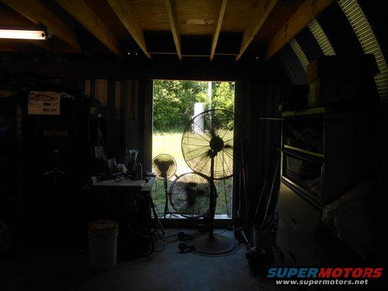 Garage interior with three industrial fans, workbench, and open doorway showing trees
