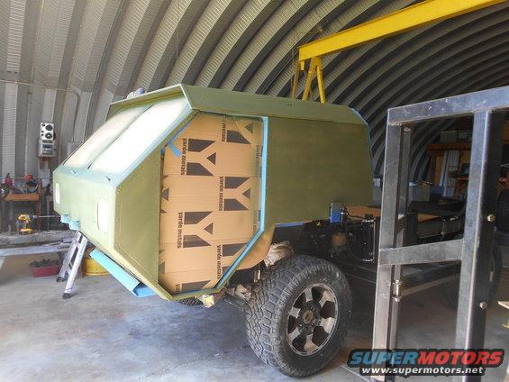 Green custom camper shell on truck chassis, side view. Cardboard boxes visible inside