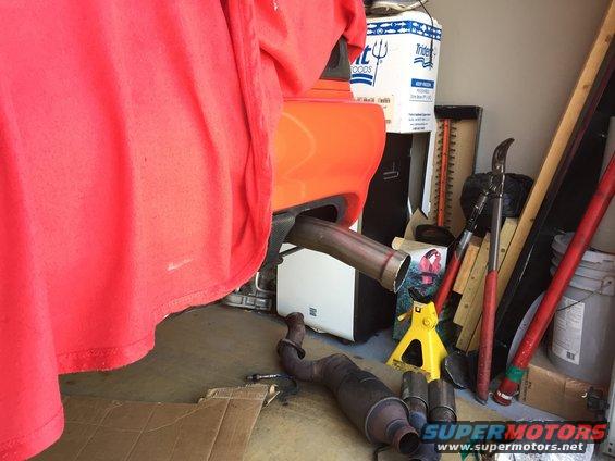 Orange car body panel with exhaust pipe removed, showing garage clutter