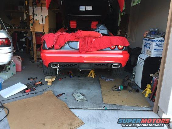 Red sports car with its rear end elevated on jack stands, covered partially with a red cloth. Exhaust pipes are visible