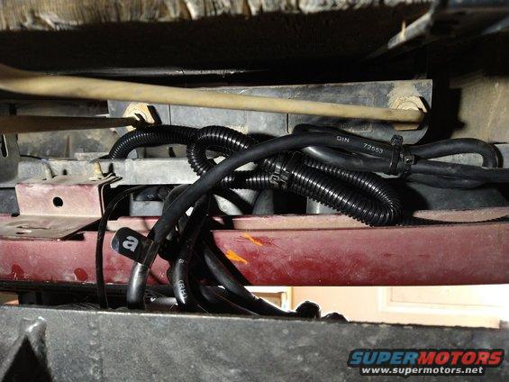 close-up of black wiring harnesses and hoses under a vehicle, some with labels
