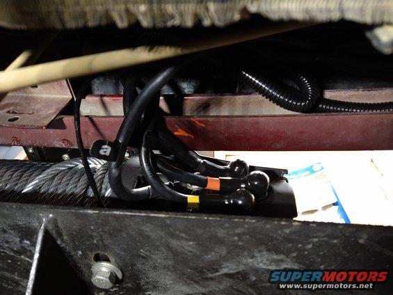 Winch cable and wiring harness with black connectors, some with orange and yellow bands, attached to a vehicle frame