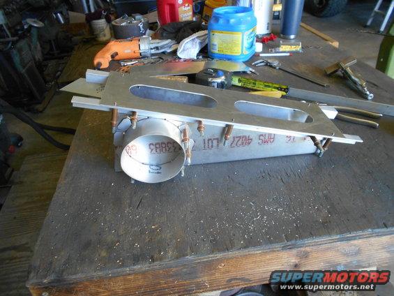 Metal fabrication part with circular opening and mounting holes on a wooden workbench with tools