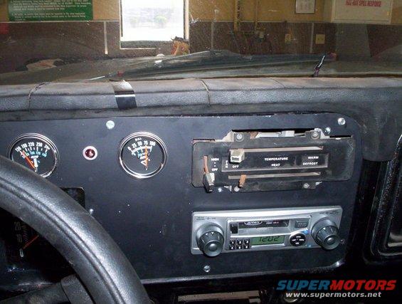 Dashboard interior with two gauges, climate controls, and an aftermarket radio displaying 12:02