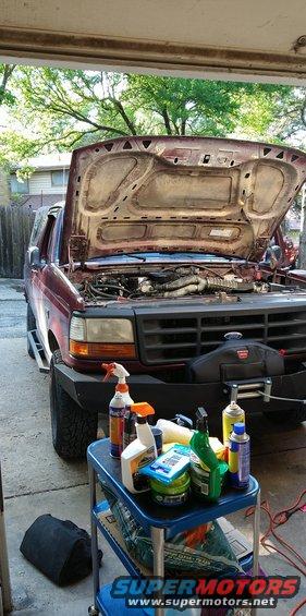 1996 Ford Bronco with hood open, showing engine and cleaning supplies on a cart