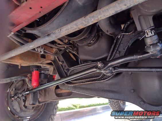 Underside view of a vehicle's suspension and drivetrain components. Red shocks are visible
