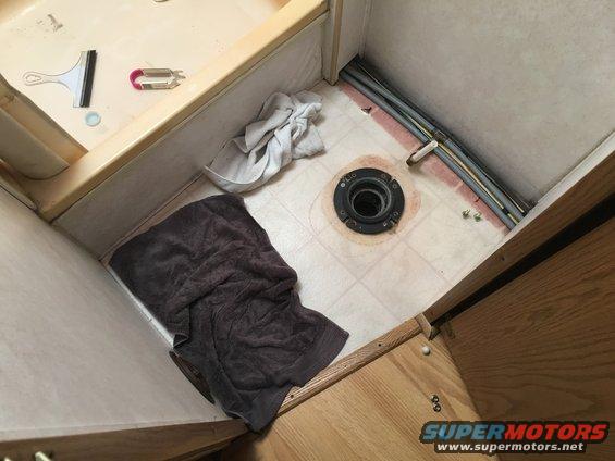 Toilet flange and plumbing pipes in a bathroom, with towels on the floor