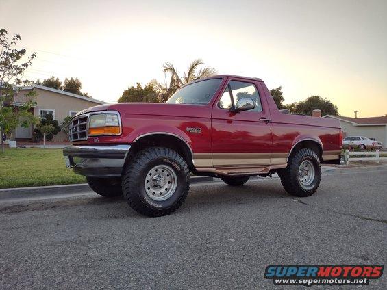 Red Ford Bronco with tan trim, lifted suspension, and aftermarket wheels parked on asphalt