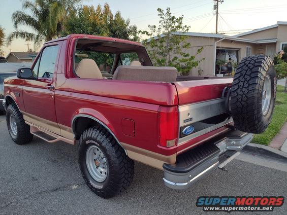 Red Ford Bronco with tan two-tone paint, spare tire on rear, viewed from the rear quarter