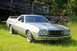 1976 Ford Ranchero - A silver 1976 Ford Ranchero is parked on a grassy area with a wooden bridge in the background.
