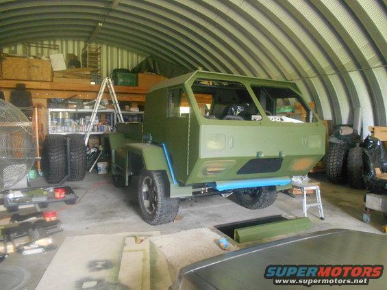Green military truck under construction in a garage, showing its front and side
