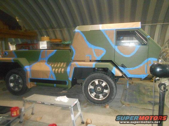 Truck in garage with camouflage paint being applied. Blue tape outlines some of the paint sections