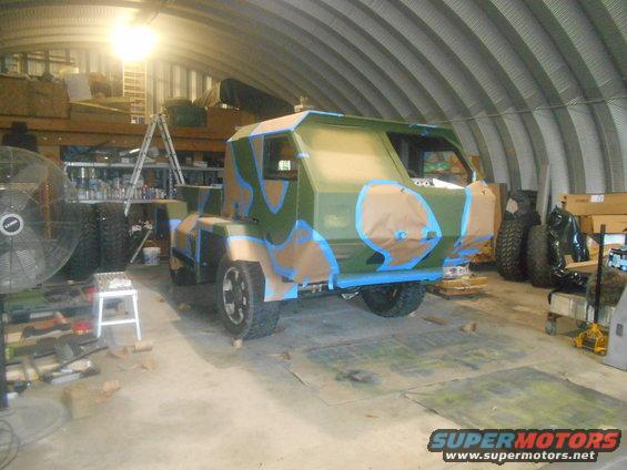Camouflaged custom vehicle in a garage, with masking tape on the body panels