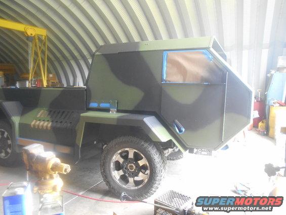 Custom truck with camouflage paint, modified body, and blue-taped windows