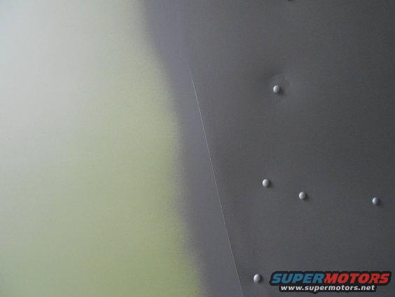 Close-up of a gray metal panel with rivets and a faint greenish area on the left