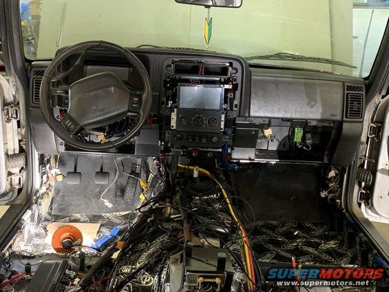 Interior of a vehicle with dashboard removed, showing exposed wiring and sound dampening material on the floor