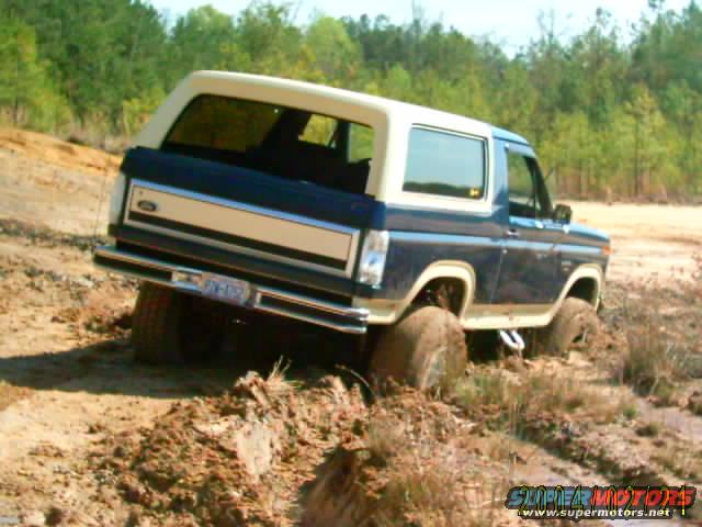 Blue and tan 1985 Ford Bronco stuck in mud, rear view with license plate visible