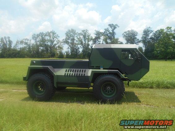Camouflaged military truck with a flatbed, parked on a grassy field