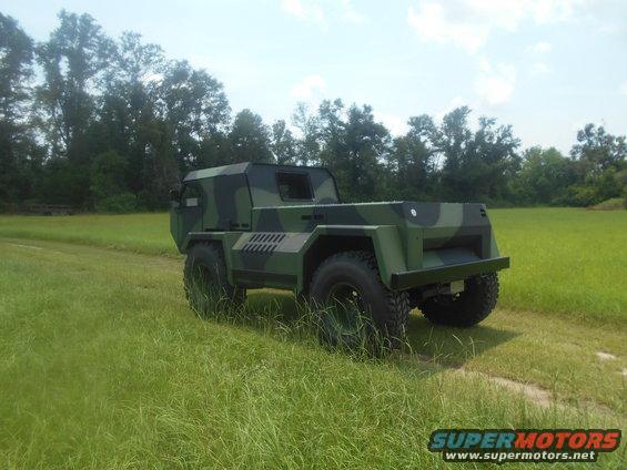 Camouflaged truck with a flatbed, parked in a grassy field
