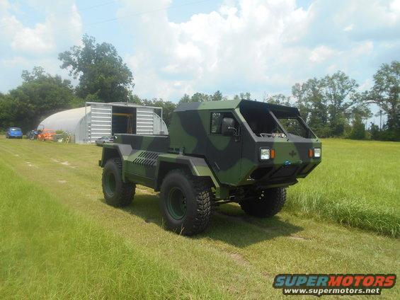 Camouflaged truck with a flatbed and large tires, viewed from a 3/4 front angle