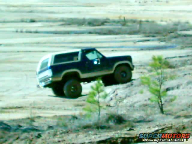 Dark blue and white SUV with off-road tires driving on a dirt hill
