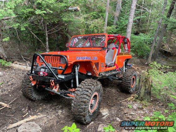 Orange Jeep with 'GENERAL LEE' on the side, modified for off-roading, driving on a dirt trail