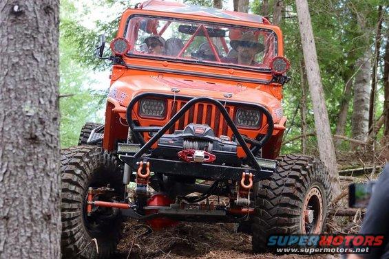 Orange Jeep Wrangler with winch and off-road tires on a wooded trail