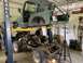 1979 Jeep CJ5 - A green Jeep CJ5 body is suspended on a lift, with its chassis and engine components laid out below in a workshop setting.