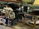 1979 Jeep CJ5 - A man sits in a chair next to a green Jeep CJ undergoing repairs in a workshop.
