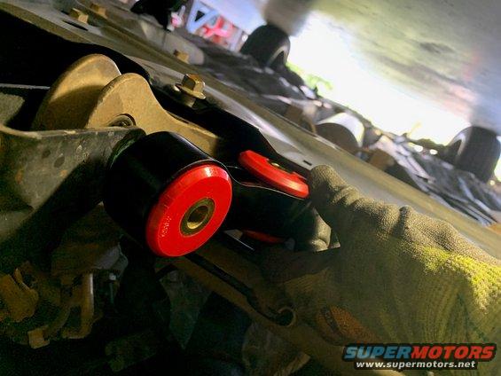 Red and black suspension bushing being installed under a vehicle