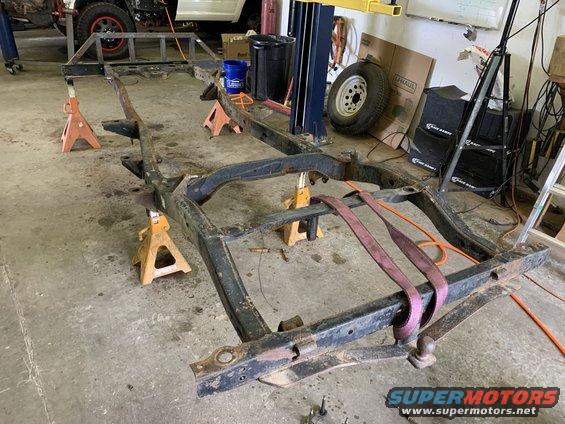 Black vehicle frame on orange jack stands, with straps and tow hitch