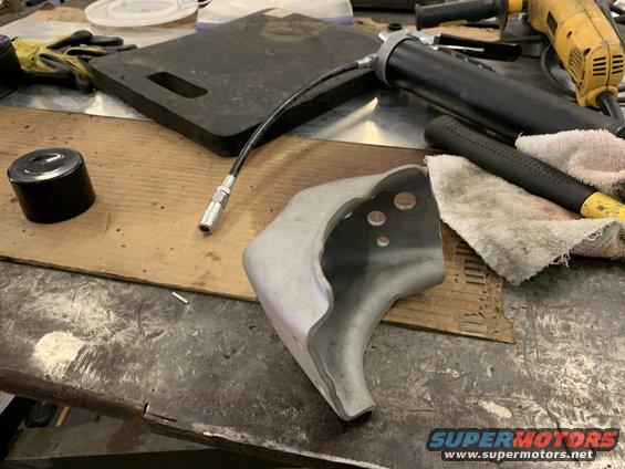 metal part on workbench with grease gun, gloves, and hammer