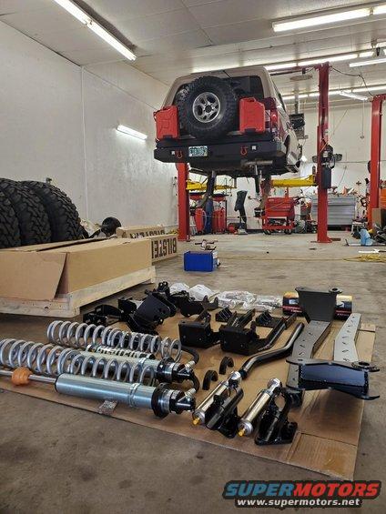 Red Ford Bronco on lift with suspension parts laid out on floor