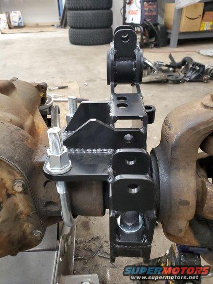 Custom suspension bracket welded to a vehicle's front axle housing, with large bolts securing it