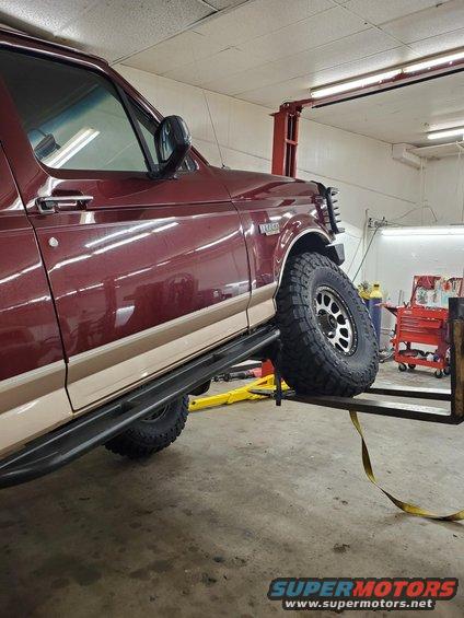 Maroon Ford Bronco on a lift, side view. It has tan trim and aftermarket wheels