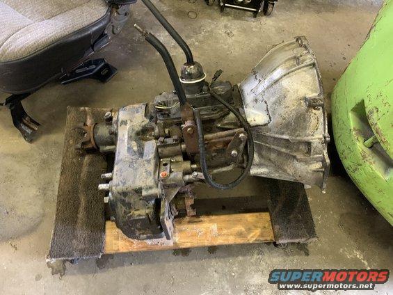 Transmission and transfer case assembly on wooden pallet, with a vehicle seat and green object in background
