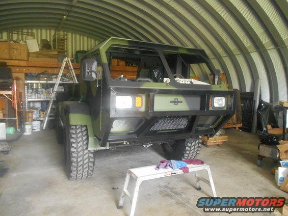 Camouflaged military truck with a large bumper and off-road tires parked inside a metal garage