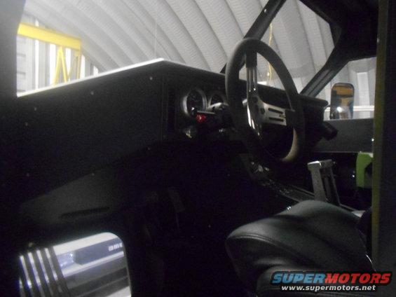 Interior view of a dark vehicle cabin, showing a steering wheel, dashboard gauges, and a gear shifter