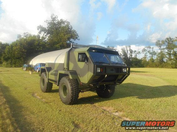 Camouflaged military-style truck with large tires parked on a grassy field
