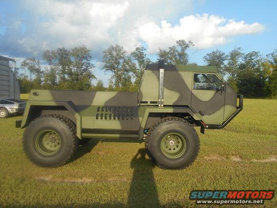 Camouflaged military truck with large tires, parked on grass