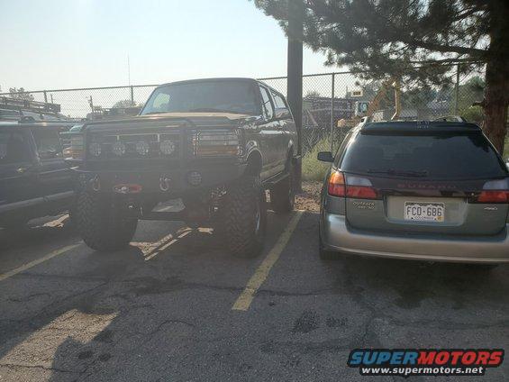 Black lifted Ford Bronco with custom bumper and lights, parked next to a Subaru Outback