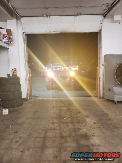 Dark Ford Bronco with headlights on, viewed from the front in a garage