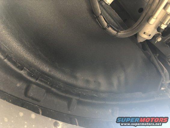 Close-up of a black plastic wheel well liner with some hoses and hydraulic lines visible above
