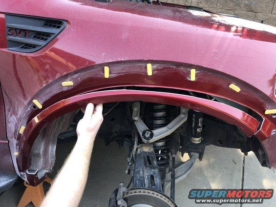 Red Ford SVT Raptor fender flare being installed, showing suspension and wheel well