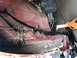 2014 Ford F-150 - The undercarriage of a red vehicle shows some damage and exposed wiring, with a jack visible.